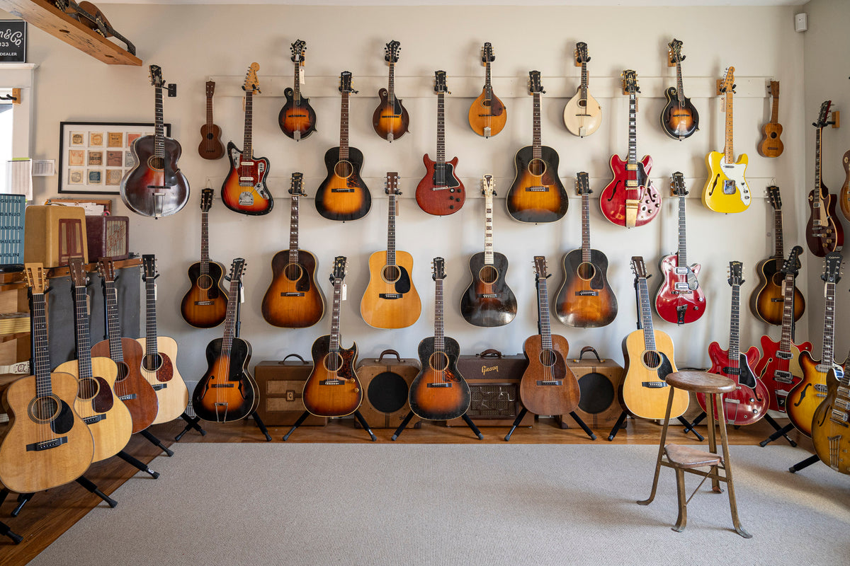 Wall displaying various vintage guitars in a room with a chair and shelves.