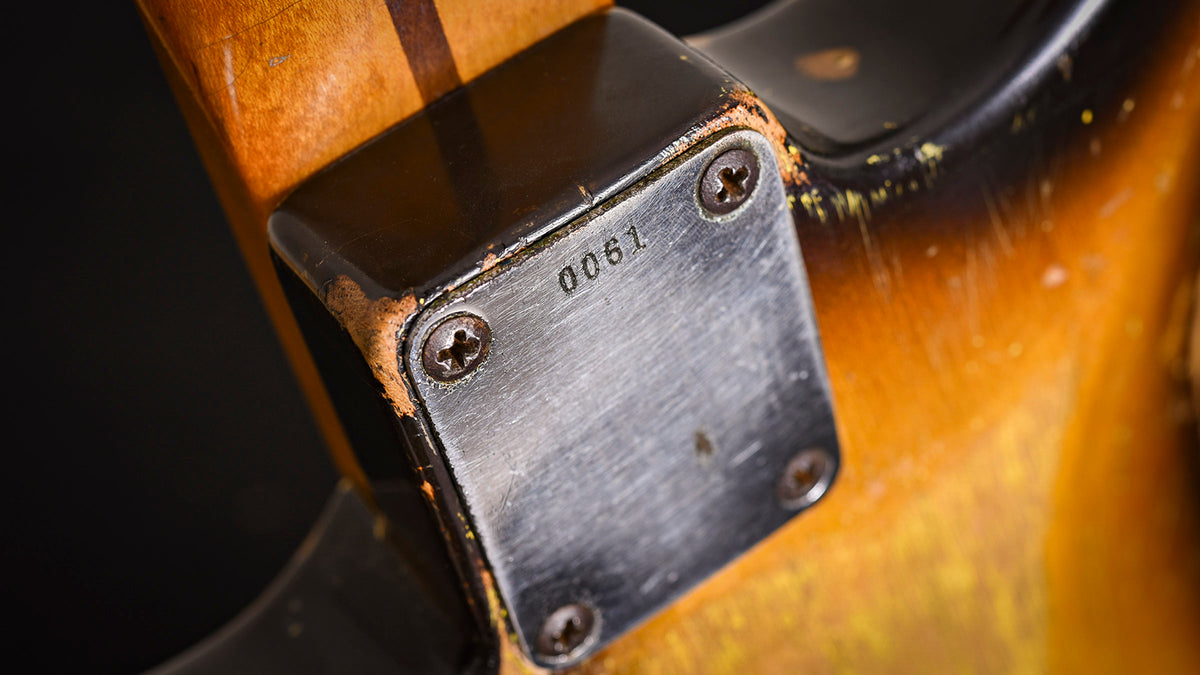 Close-up of a vintage Fender stratocaster guitar's neck plate with visible serial number.