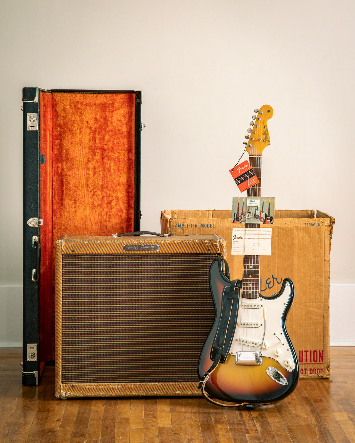 Vintage Fender Stratocaster guitar with vintage Fender Tremolux amplifier and case on a wooden floor