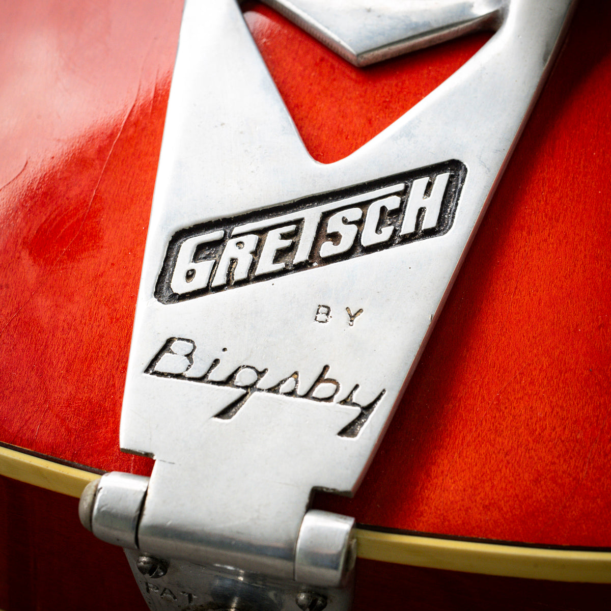 Close-up of a vintage Gretsch by Bigsby tremolo system on a red guitar body.
