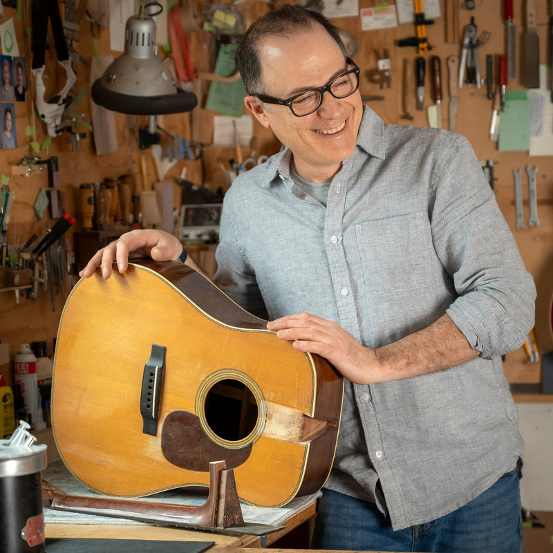 Man holding a vintage Martin D-28 acoustic guitar in a workshop setting