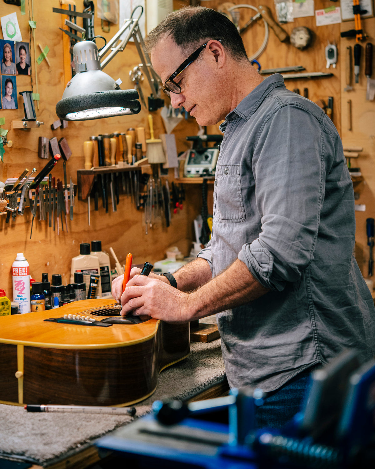 Man working on a vintage Martin guitar in Folkway Music's workshop with tools and equipment around.