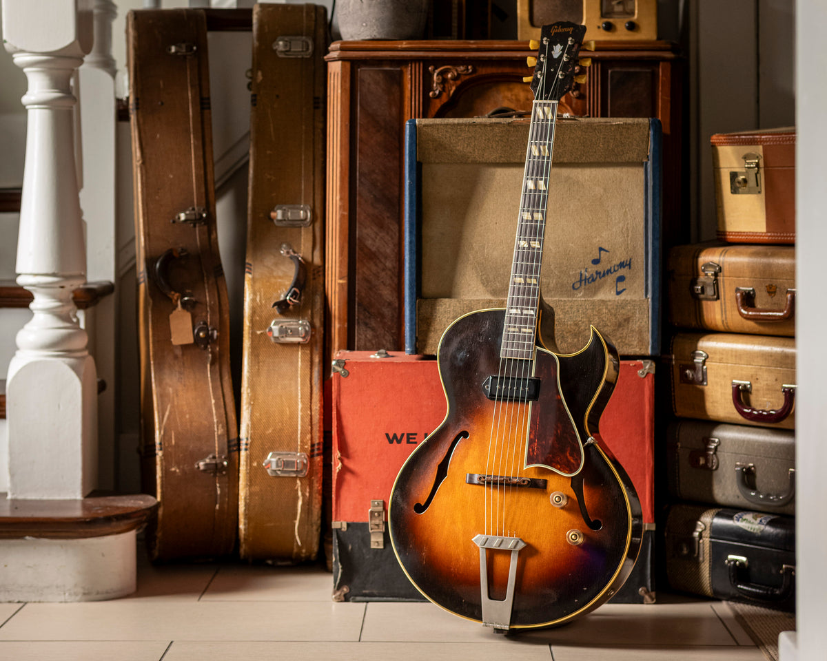 Vintage Gibson electric guitar leaning against vintage amplifiers and suitcases.  