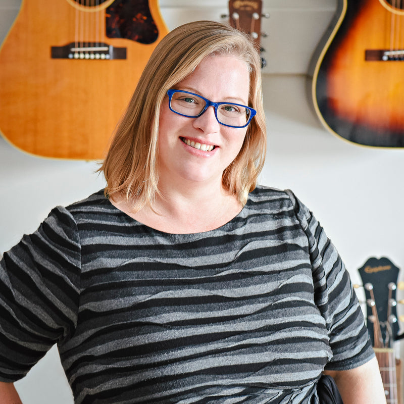 Woman wearing glasses and a striped shirt with guitars in the background