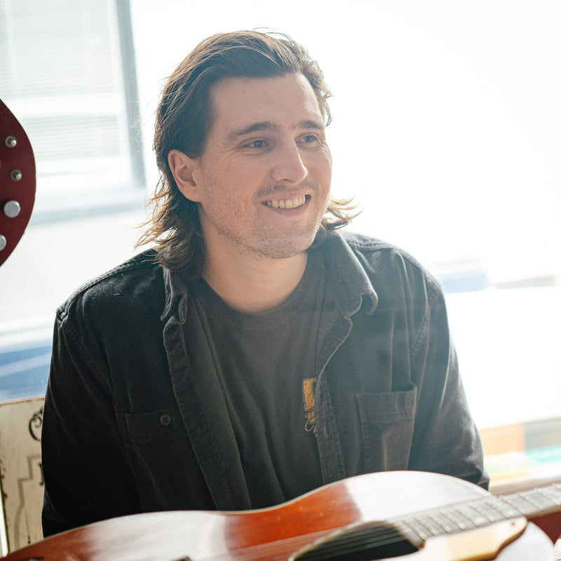 Man holding an vintage Gretsch acoustic guitar indoors with a blurred background