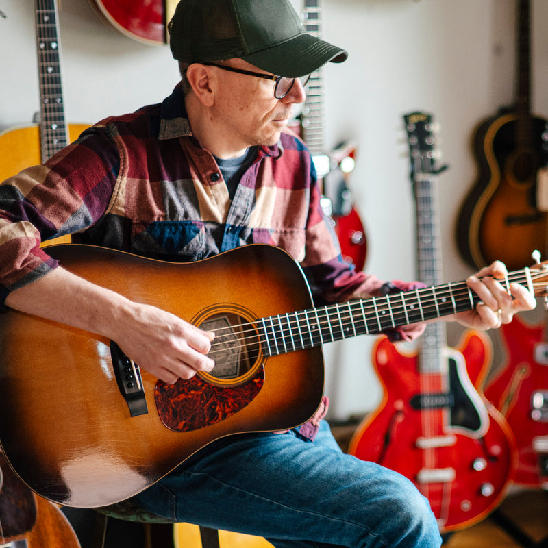 Man playing an acoustic guitar in a room with guitars on the wall