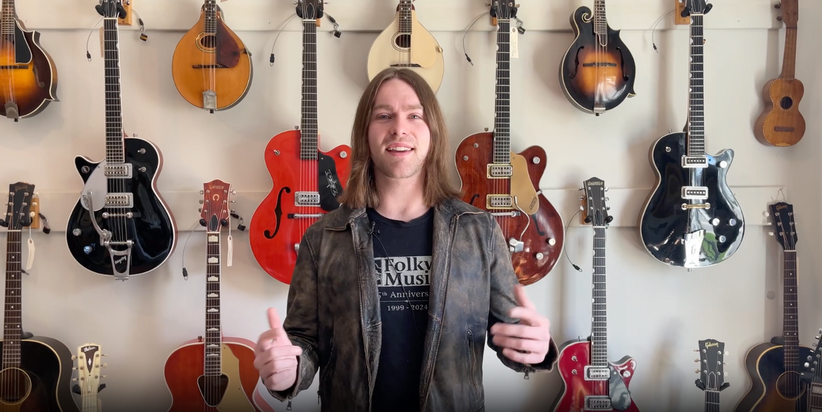 Video of a man in front of a wall of vintage guitars.  